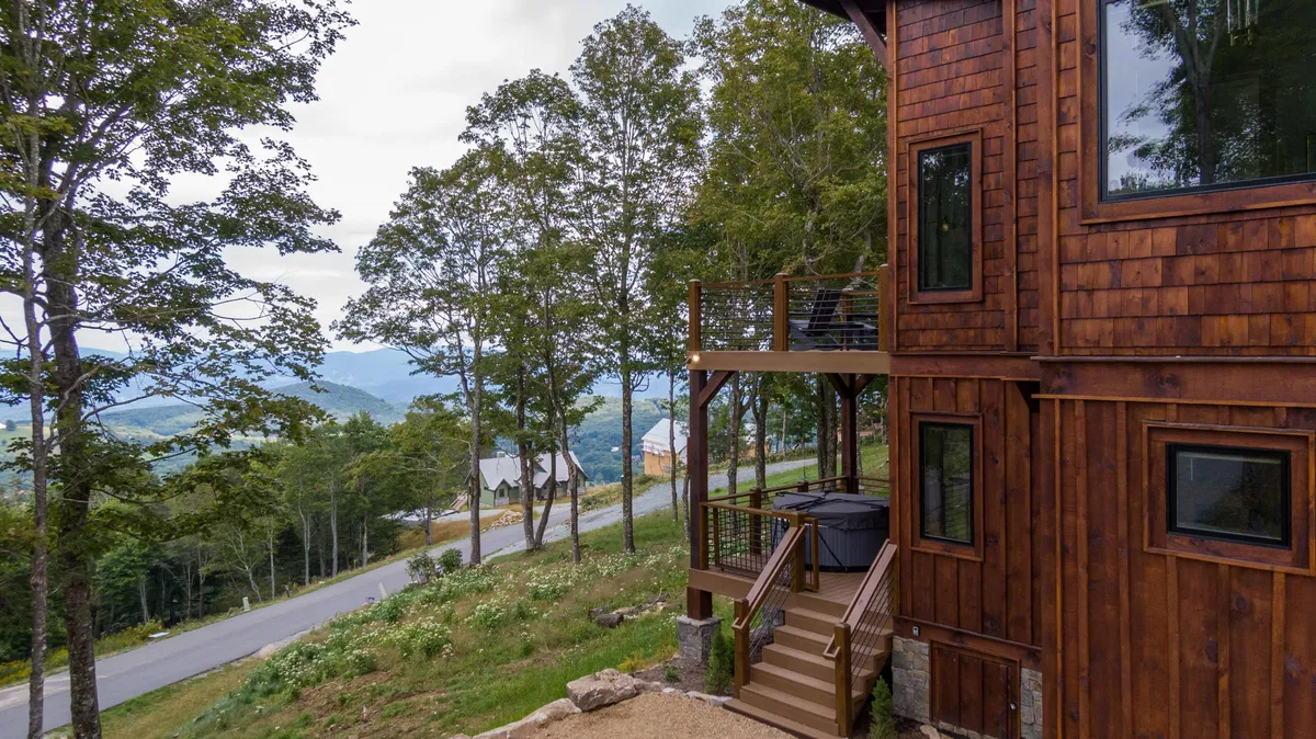 A wide shot of the deck reveals both the hot tub and outdoor seating, set against the backdrop of the cabin’s wooden exterior and mountain views beyond. The layout highlights spaces perfect for socializing, relaxing, and taking in the surrounding scenery.