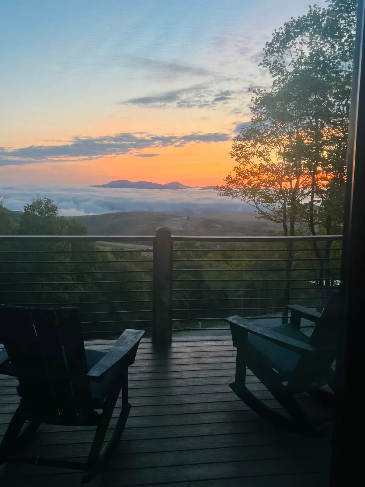 A tranquil mountain deck at sunset, with inviting deck chairs perfectly positioned to capture sweeping views of the surrounding peaks and lush forest. The soft glow of the setting sun bathes the scene, promising a peaceful spot for couples to unwind, relax, and enjoy the serenity of nature.