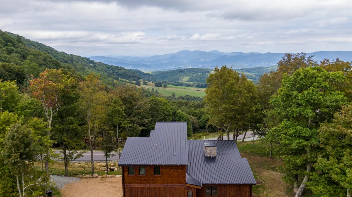 The exterior of the property is nestled among towering trees with mountains rising in the background. The porch offers a tranquil spot to take in sunrise views, stargaze at night, or simply connect with the natural surroundings.