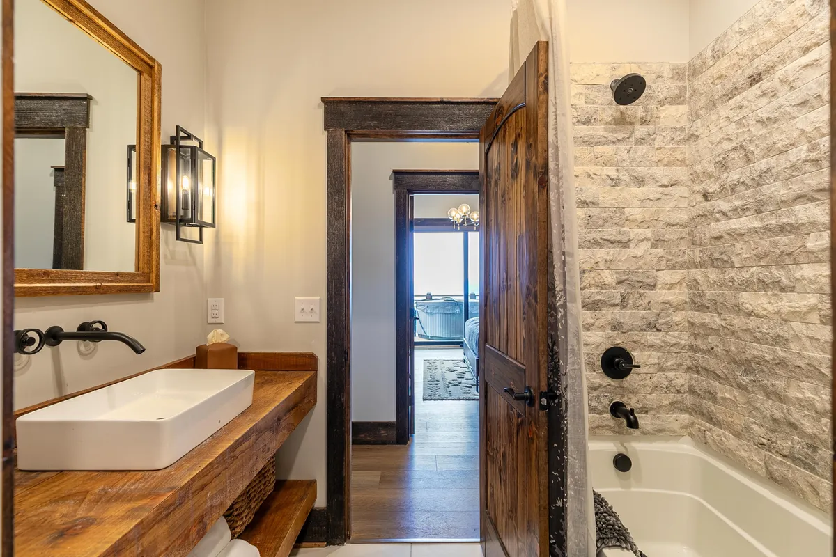 A stylish full bathroom with a wooden vanity, stone shower wall, framed mirror, and matte black fixtures. The space feels modern yet cozy, offering a welcoming atmosphere for guests to refresh after a day of adventure.
