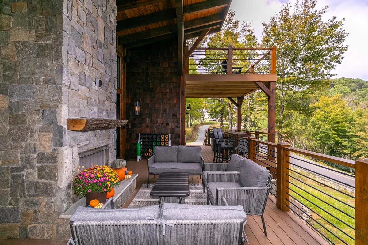 This image features a spacious outdoor seating area centered around a stone fireplace, accented with a beautiful flower arrangement and bordered by a wooden railing. The inviting setup is perfect for gatherings or relaxing evenings, with the warmth of the fireplace and an open-air ambiance.